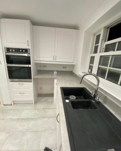 A new modern kitchen installation featuring white laminate flooring, grey kitchen countertops and white kitchen cabinets and cupboards and a black composite sink.