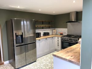 A new kitchen installation featuring patterned flooring, white kitchen cabinets, wooden worktops and white wall tiling.