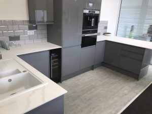 A new commercial kitchen installation featuring grey kitchen cupboards and cabinets, white worktops, integrated appliances and vinyl flooring.