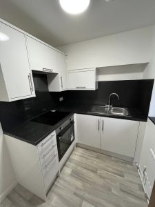 A new kitchen installation featuring white cabinets and cupbaords, grey vinyl flooring, black worktops and black wall tiling.