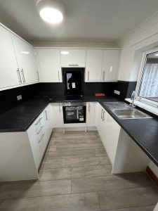 A new kitchen installation featuring white cabinets and cupboards, grey vinyl flooring, black worktops and black wall tiling.