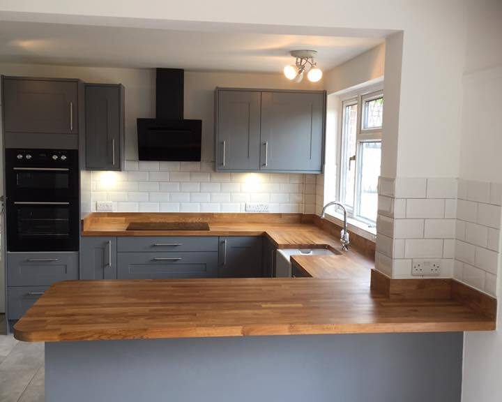 A kitchen installation featuring white wall tiling, grey kitchen cabinets, integrated appliances and wooden worktops.