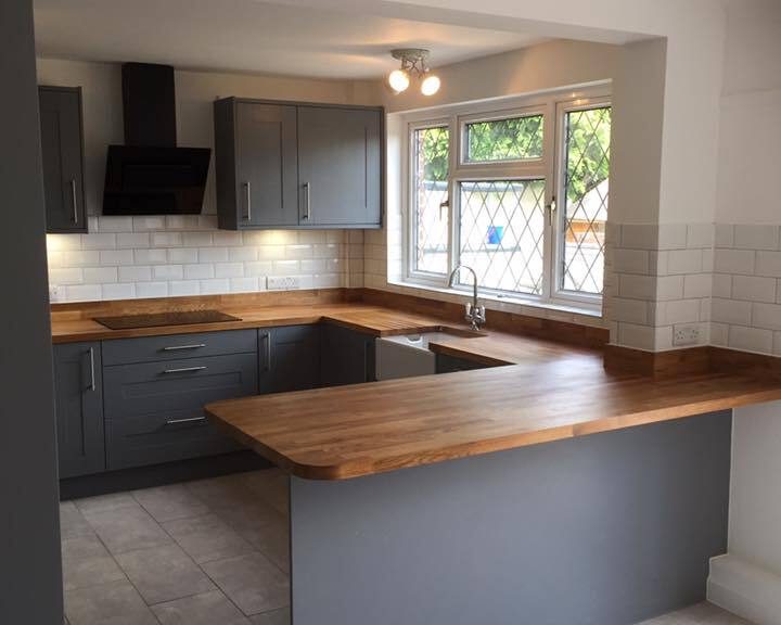 A kitchen installation featuring white wall tiling, grey kitchen cabinets, integrated appliances and wooden worktops.