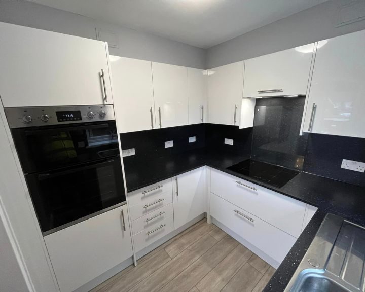 A new kitchen design by Basingstoke Bathroom Fitters that includes white kitchen cabinets, integrated appliances, black countertops and black wall tiling.