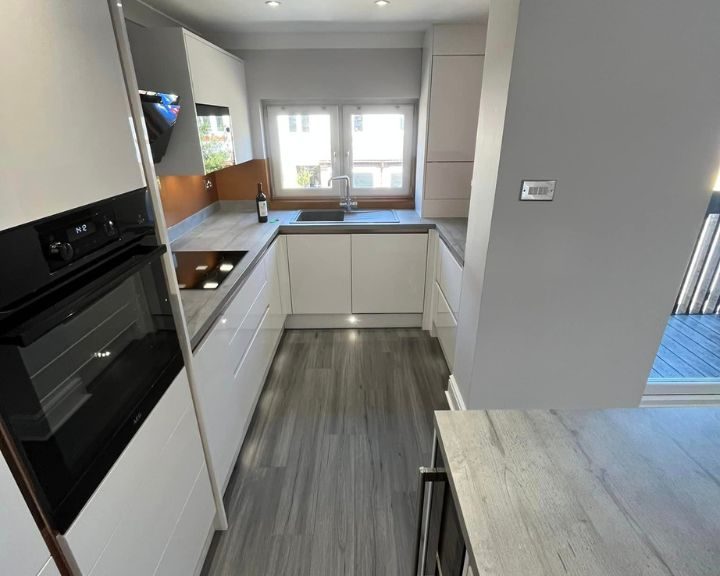 A new kitchen design by Basingstoke Kitchen Fitters that includes grey vinyl flooring, integrated cooker, white kitchen cabinets and cupboards and grey wooden countertops.