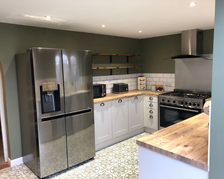 A new kitchen installation featuring white wall tiling, vinyl patterned flooring, white kitchen cabinets and wooden countertops.