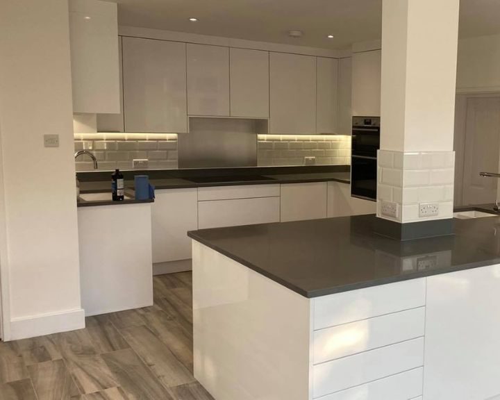 A kitchen that has been refurbished with new white painted cupboards and cabinets, new grey countertops and wooden vinyl flooring.