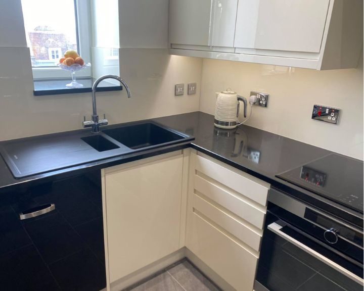 A kitchen that has been refurbished with new cupboard doors, a new sink and grey countertops.