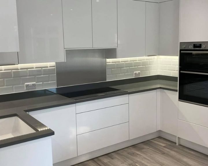 A new modern kitchen that has been installed with new white tiling, white kitchen cabinets and cupboards, vinyl flooring and grey kitchen countertops.